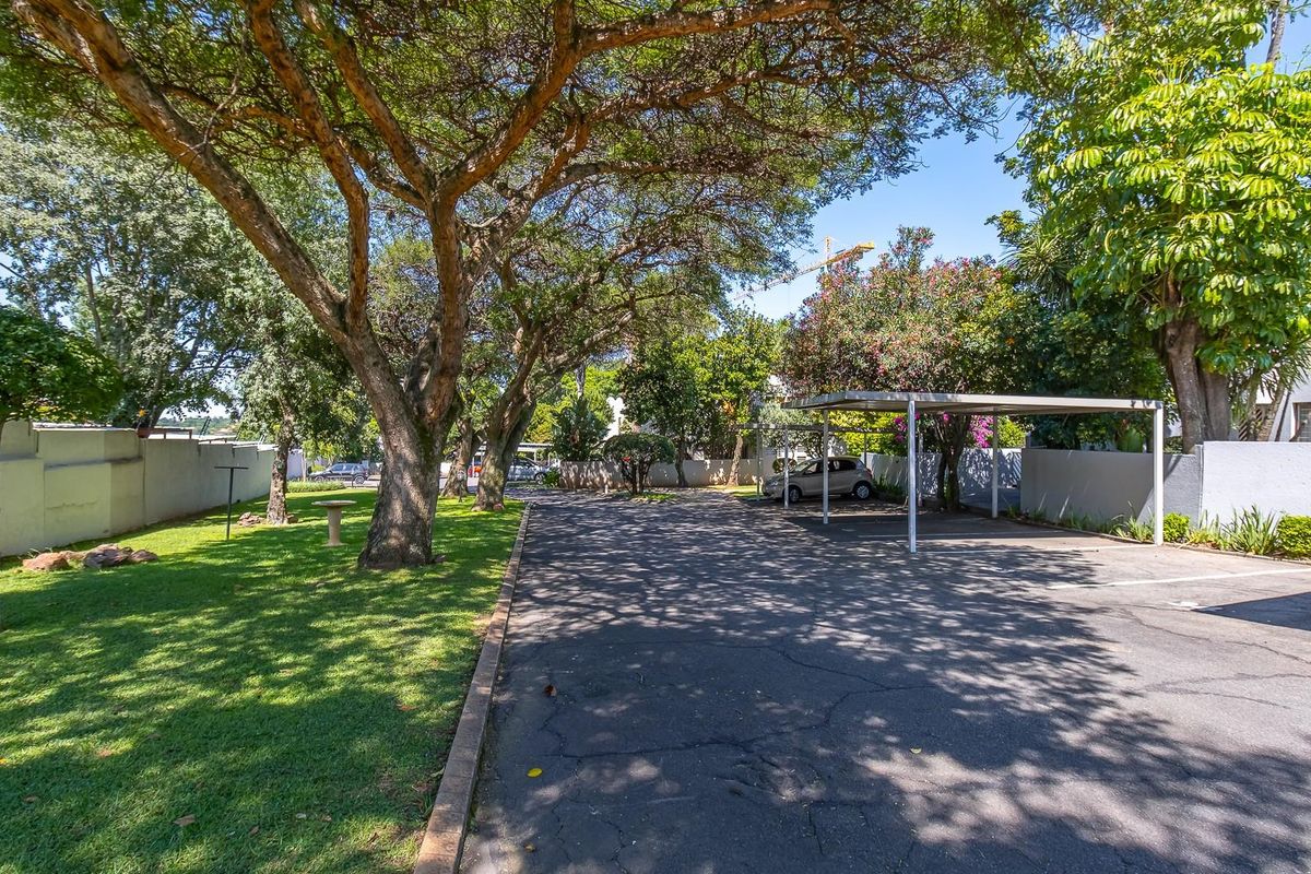 A well-maintained outdoor parking area featuring covered carports, mature trees, and a landscaped lawn within the apartment complex grounds.