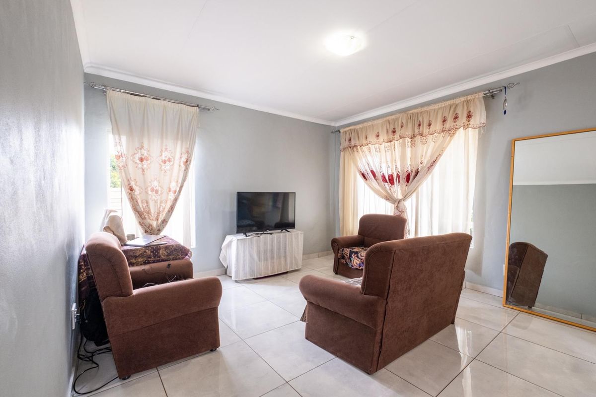 A bright living room featuring neutral tiled flooring, coved ceilings, and large windows with curtain tracks, providing a functional and well-lit living space.