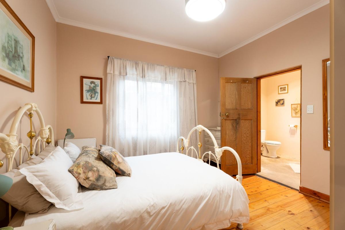 A bedroom featuring polished timber flooring and an en-suite bathroom with a toilet, showcasing a classic interior layout.