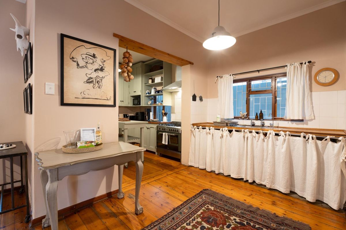 A rustic kitchen featuring timber flooring, open shelving, a gas stove, and a farmhouse-style sink with a curtained base.