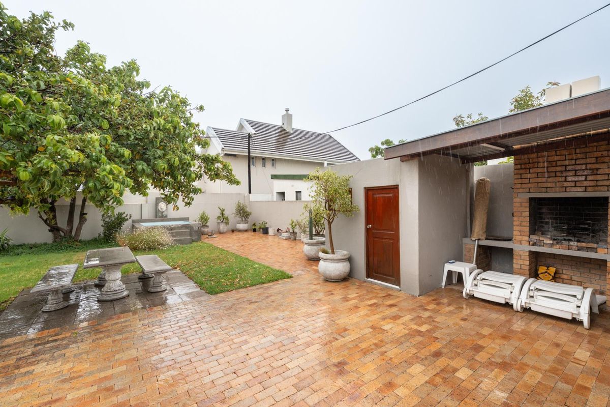 A private rear garden featuring a paved patio area, built-in brick braai, and a small water feature, ideal for outdoor entertaining.