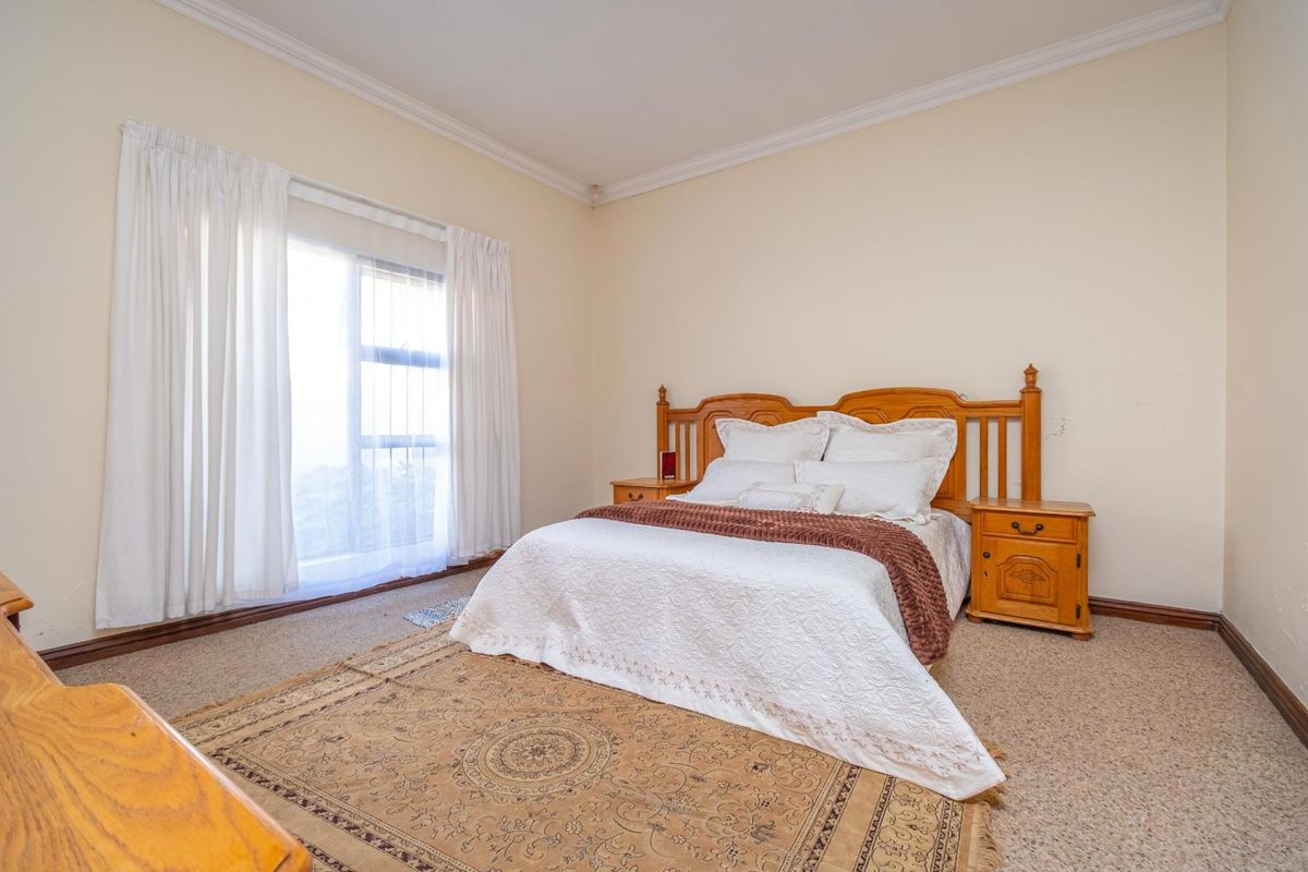 A spacious bedroom featuring neutral wall tones, carpeted flooring, and a large window with natural light.