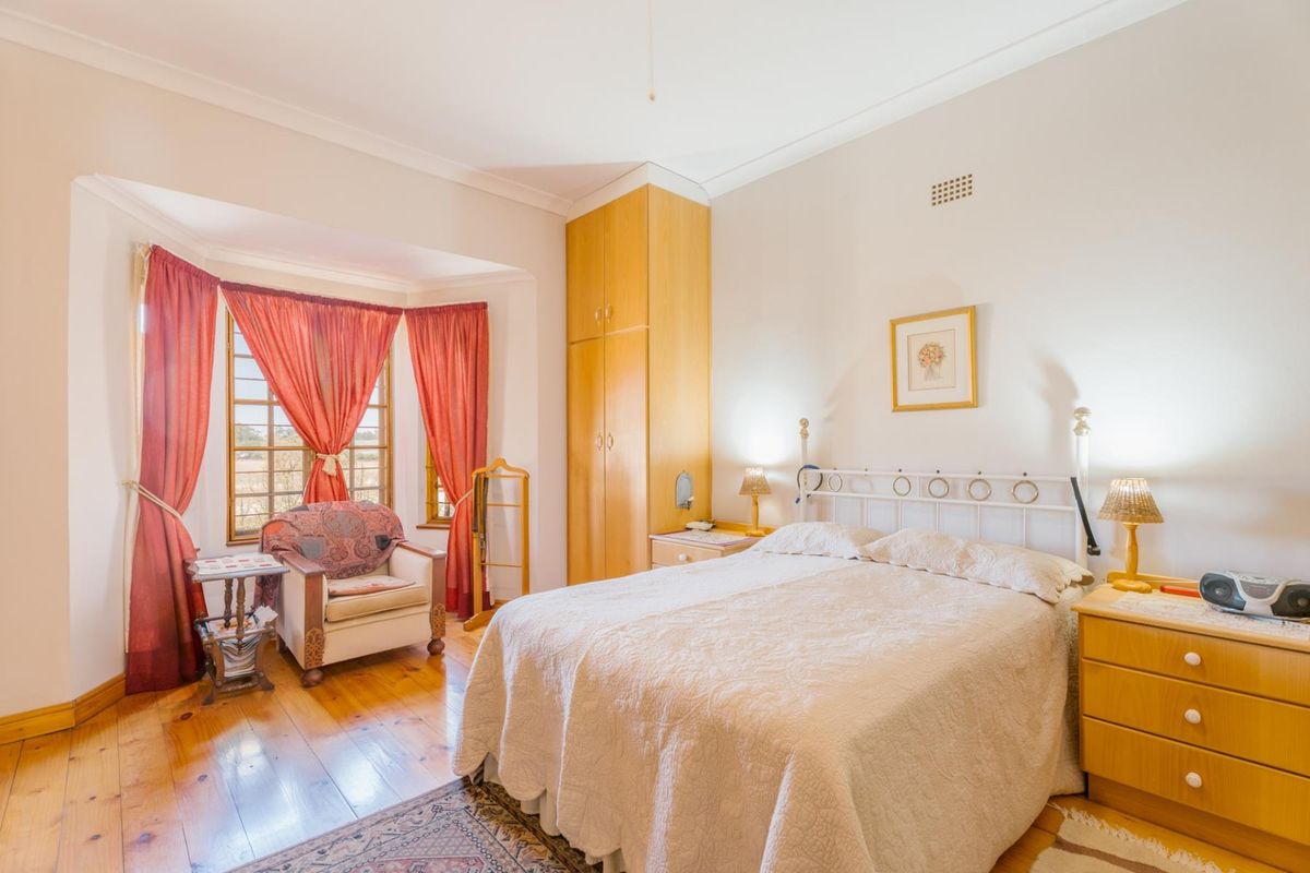 A well-lit bedroom featuring polished timber flooring, a built-in wooden wardrobe, and a bay window that provides natural light.