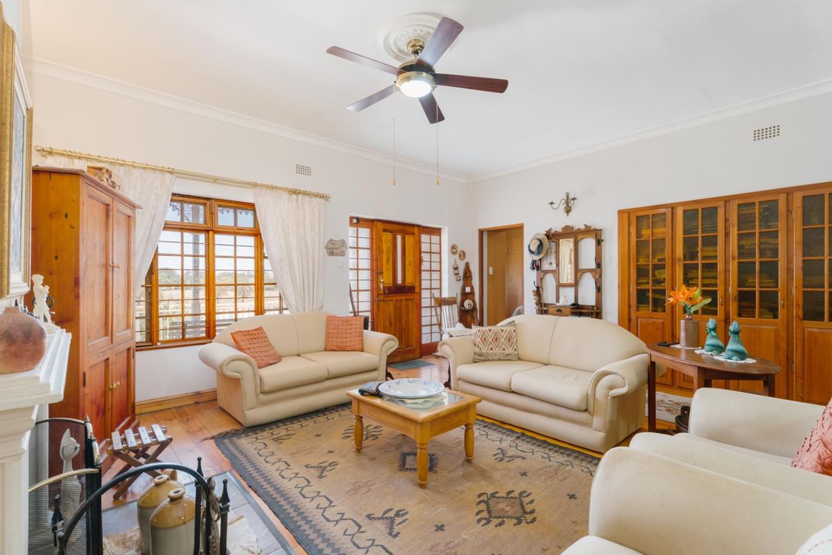 A spacious living room featuring timber flooring, a ceiling fan, and built-in wooden cabinetry, offering a warm and traditional aesthetic.
