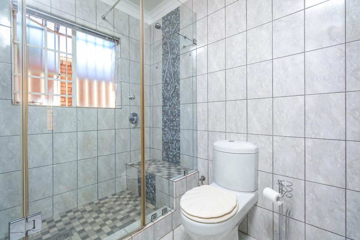 A functional bathroom featuring a glass-enclosed shower with mosaic tile accents, a built-in shower bench, and a standard toilet.