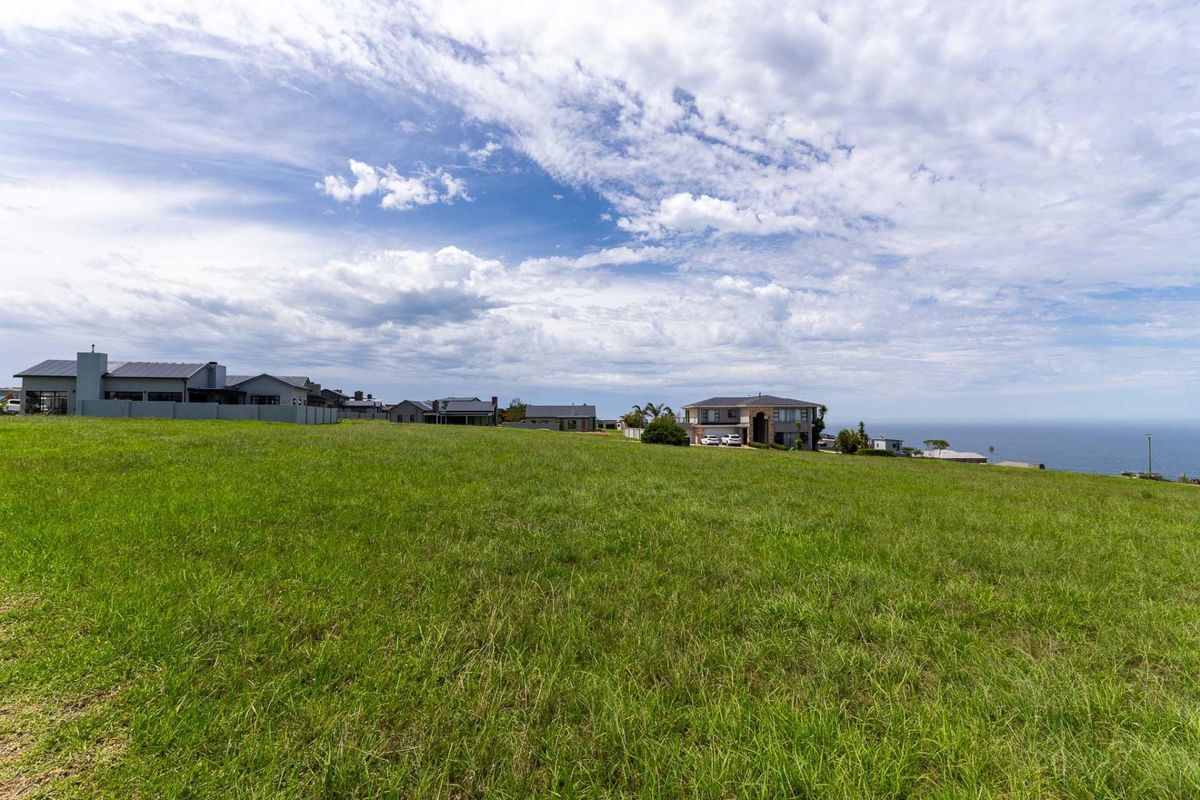 A spacious, vacant residential plot featuring expansive grassy terrain with scenic coastal views and surrounding established neighborhood homes.