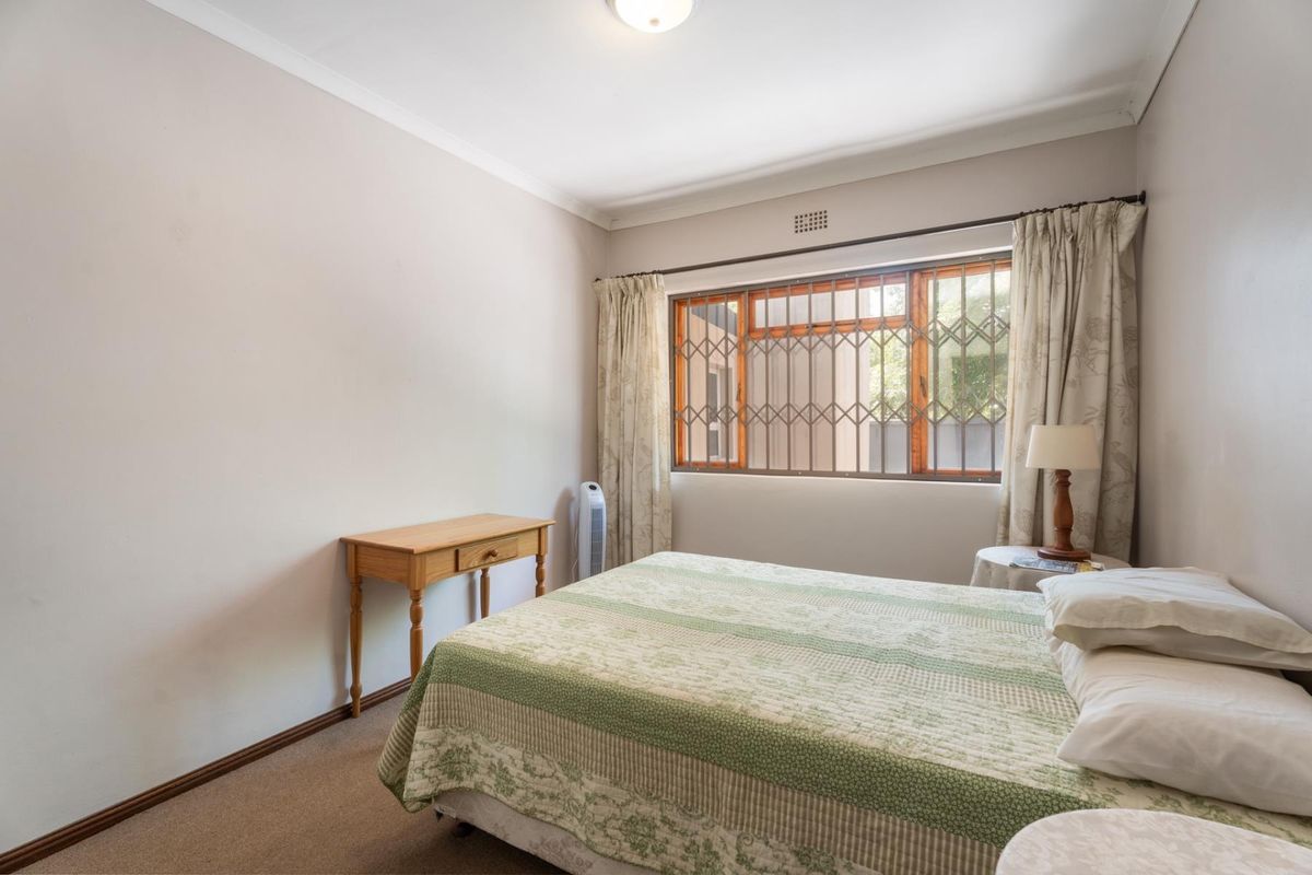 A functional bedroom featuring neutral wall tones, carpeted flooring, and a window fitted with security bars.