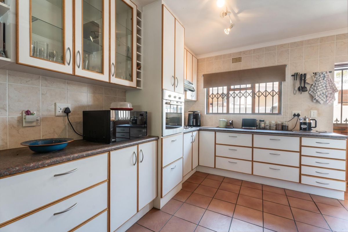 A functional kitchen featuring white cabinetry with wood trim, tiled splashbacks, terracotta floor tiles, and a built-in oven.