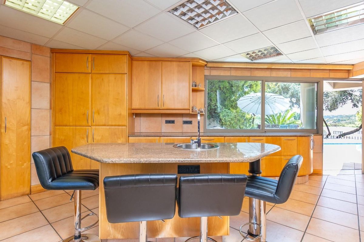 A spacious kitchen featuring light wood cabinetry, a central island with a granite countertop, and large windows overlooking the outdoor pool area.