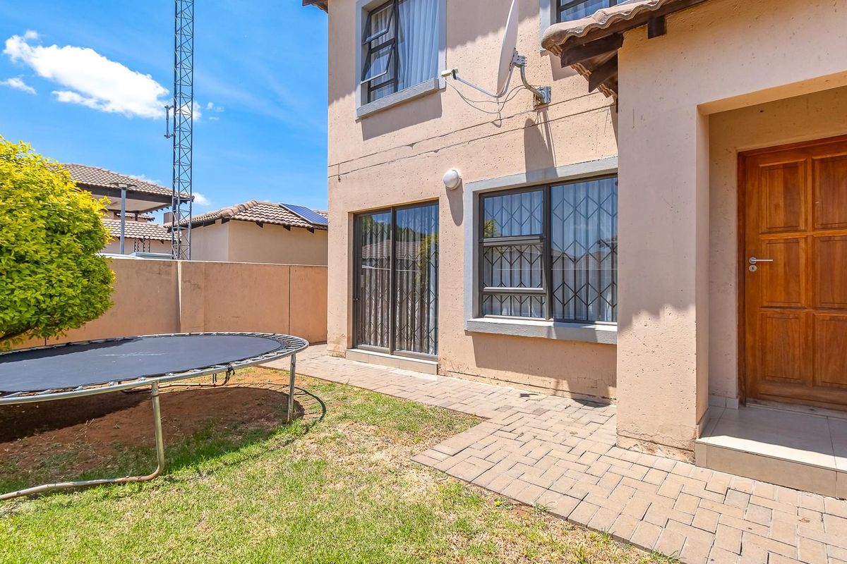 Rear exterior view of the townhouse featuring a paved patio area, small garden, sliding glass doors, and a wooden entrance door.