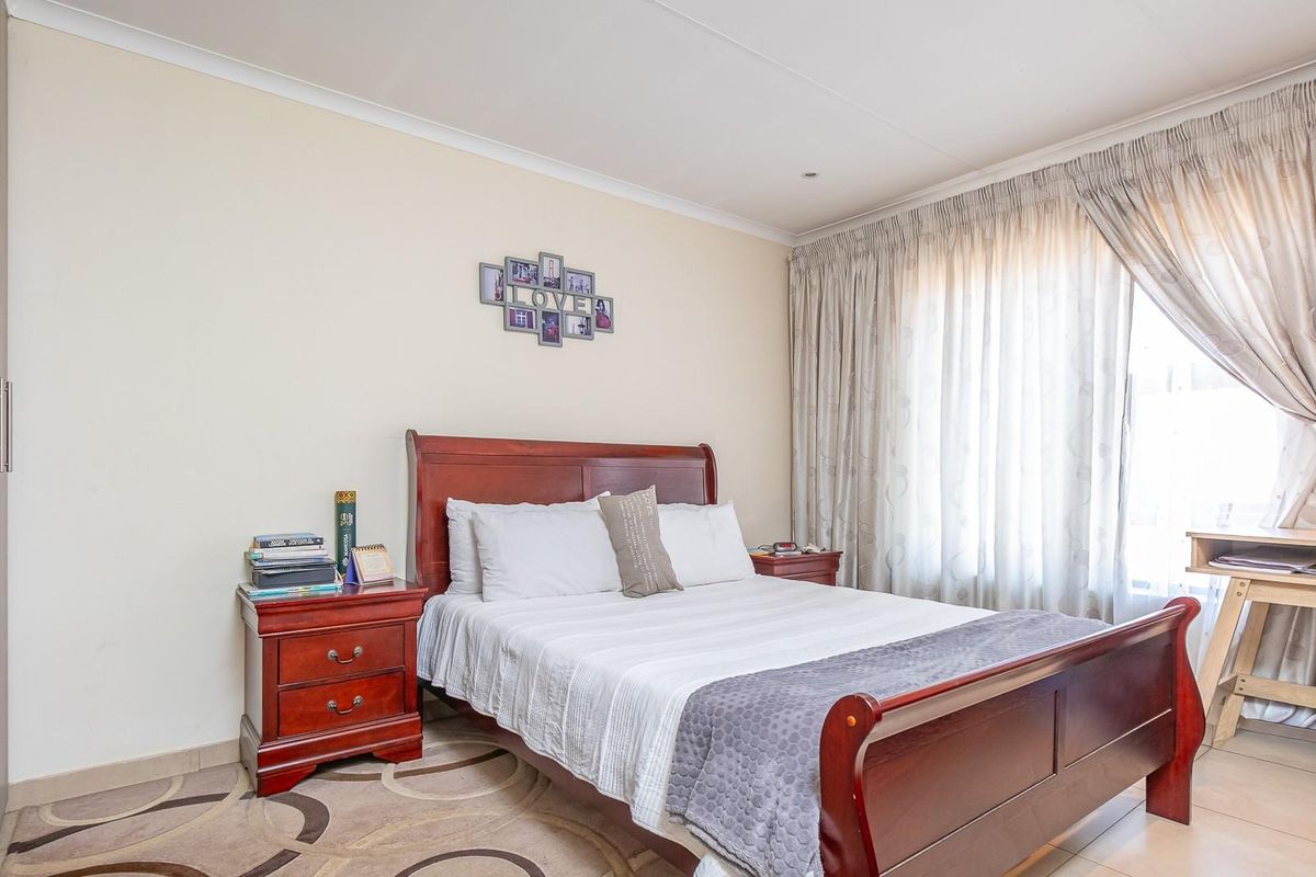 A well-lit bedroom featuring built-in cupboards, tiled flooring, and large windows with curtain tracks.