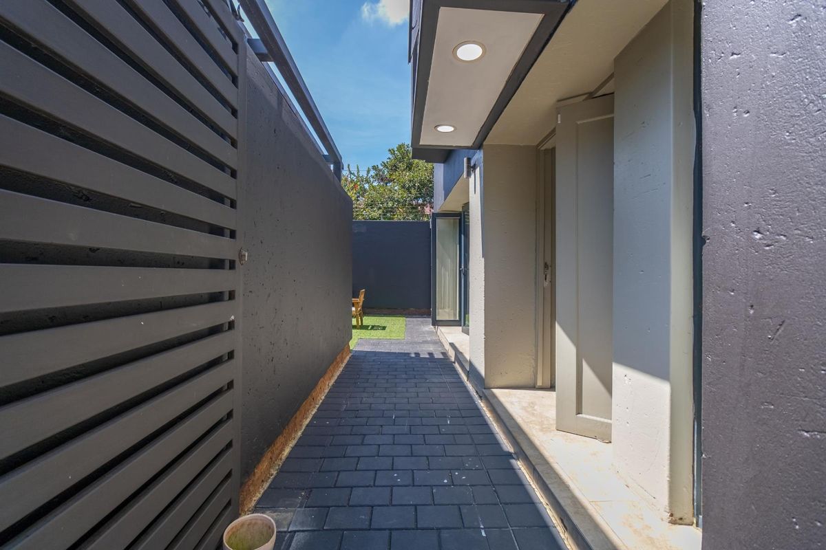 A side walkway featuring dark paved flooring, modern recessed ceiling lighting, and a slatted privacy screen leading toward a rear garden area.
