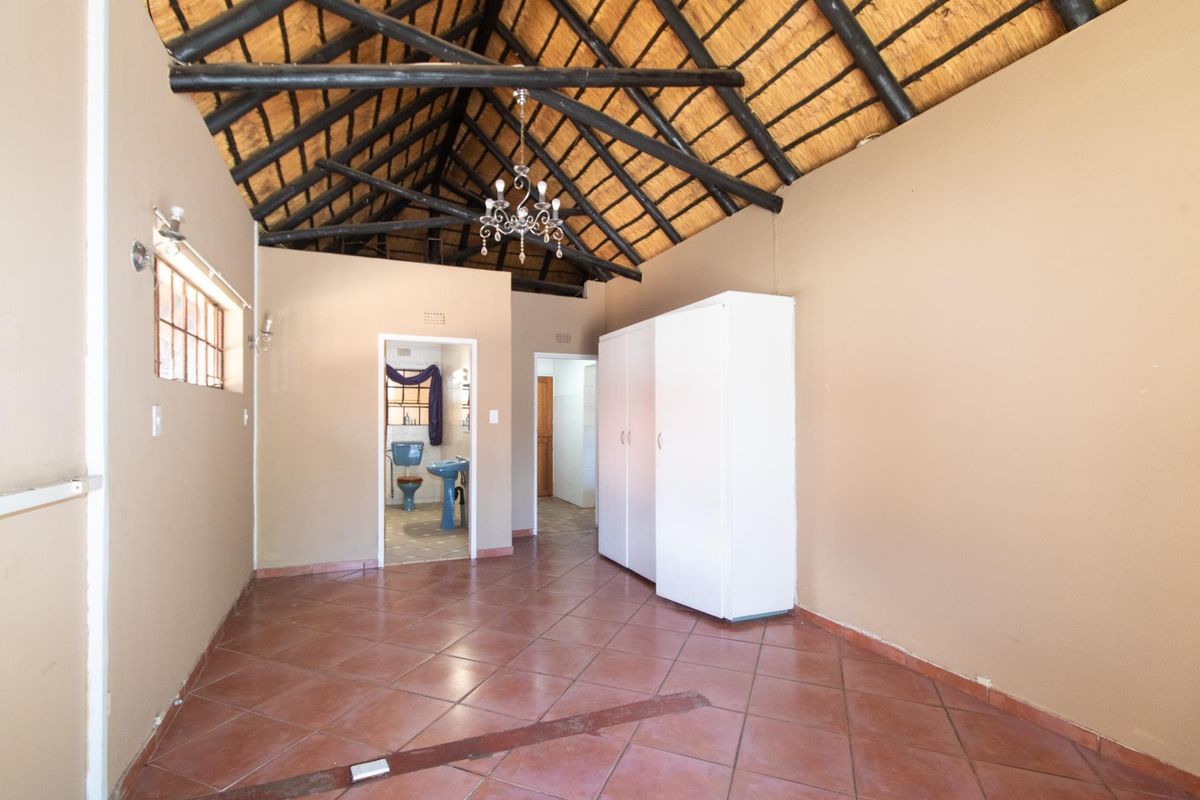 Bedroom featuring a high vaulted thatched ceiling with exposed timber beams, tiled flooring, and an en-suite bathroom with dated sanitary ware.