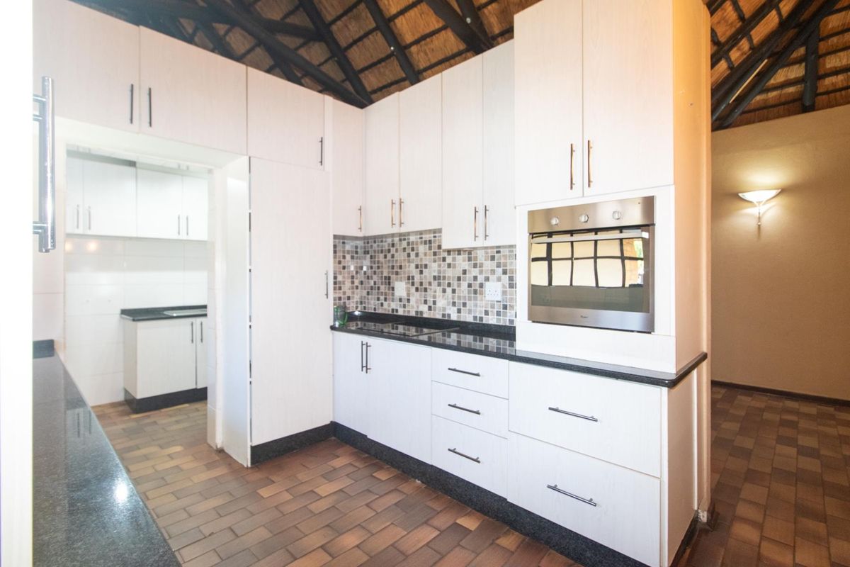 A well-maintained kitchen featuring light-toned cabinetry, dark granite countertops, a mosaic tile backsplash, and a built-in oven, with an adjacent scullery area.