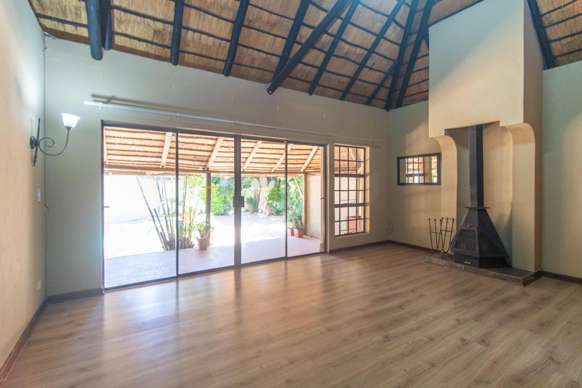 Spacious living room featuring a high vaulted thatched ceiling, wood-look flooring, a built-in fireplace, and large sliding glass doors opening to a patio.