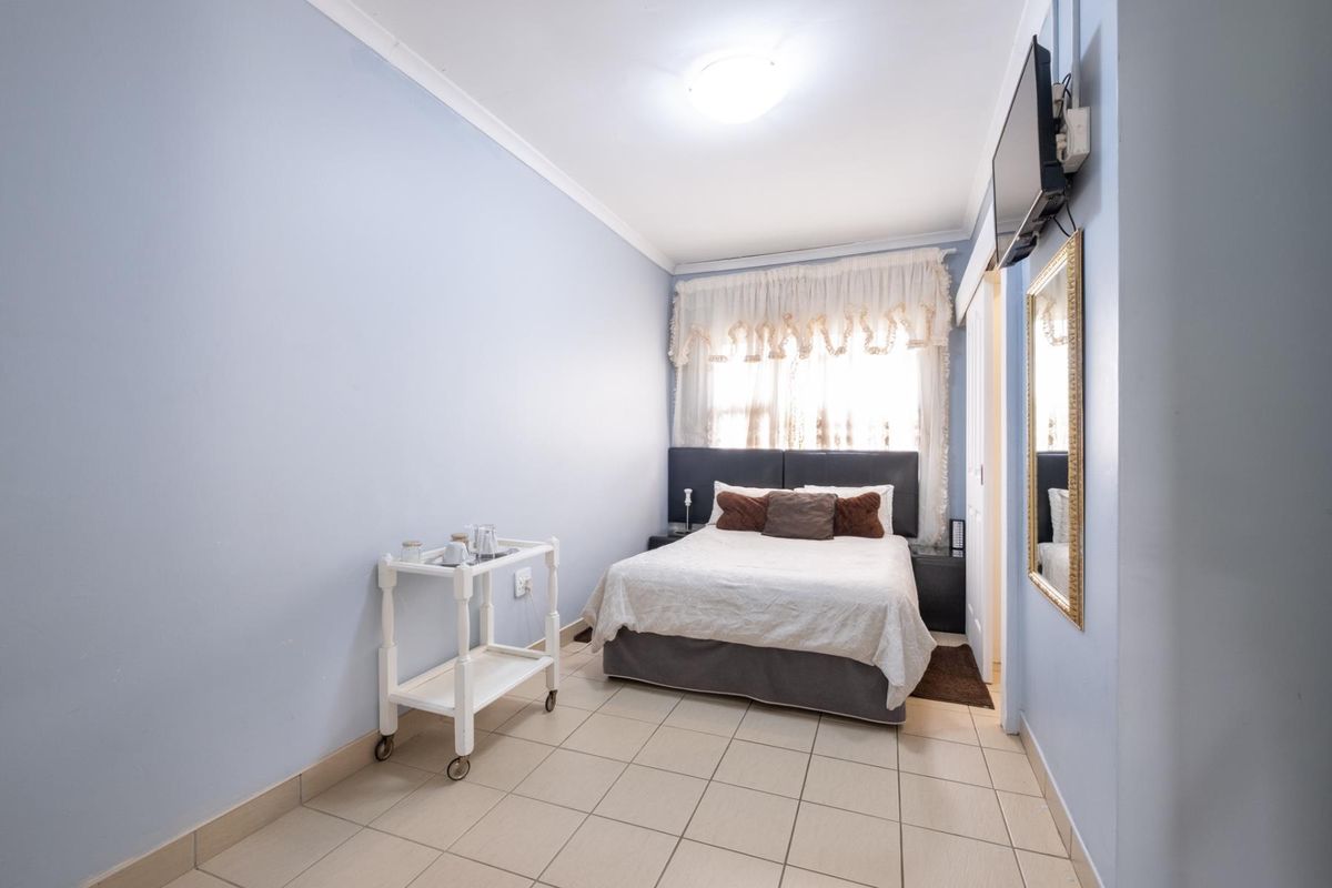 A functional bedroom featuring tiled flooring, neutral wall finishes, and a window with privacy curtains.