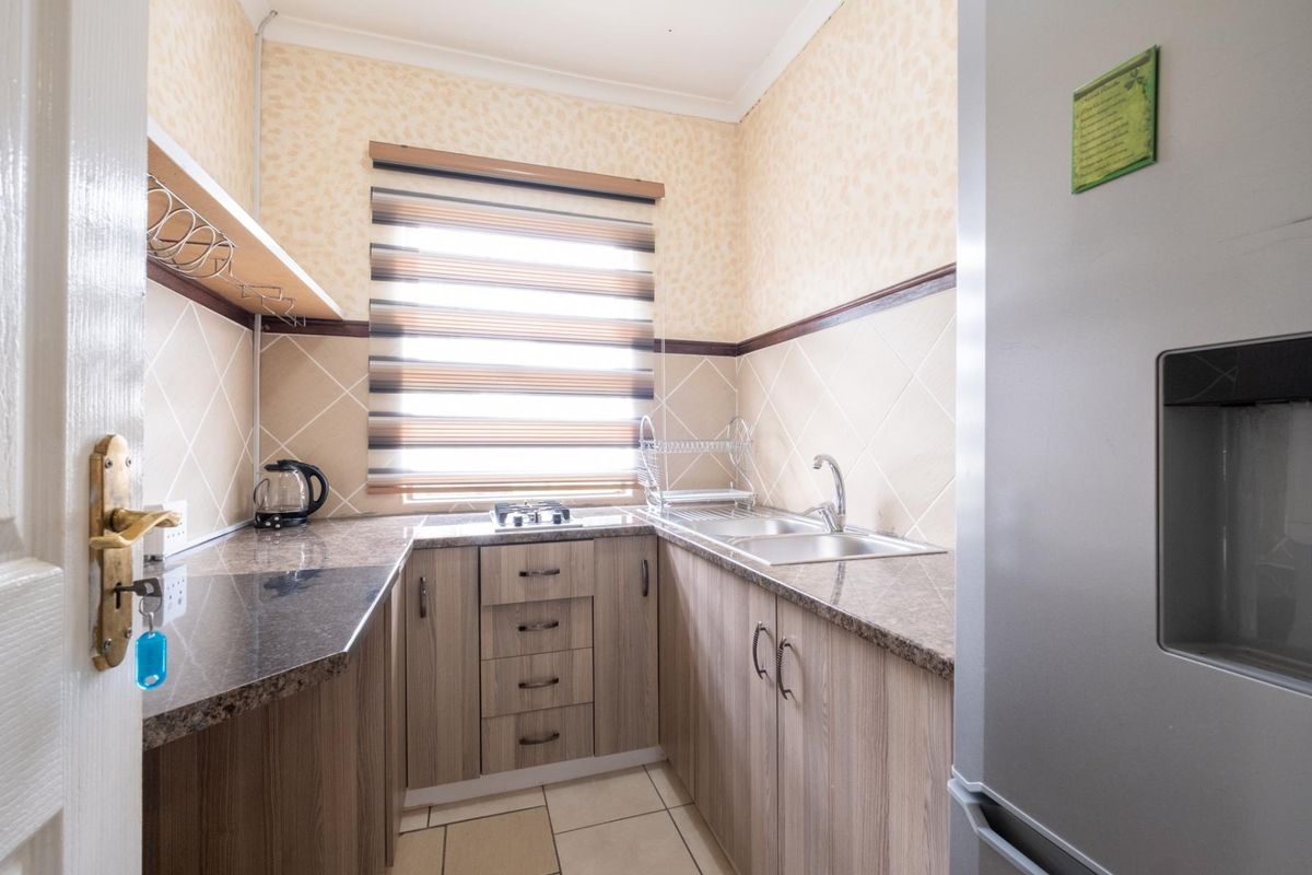 Compact kitchen featuring granite countertops, wood-finish cabinetry, a stainless steel double sink, and a built-in gas hob.