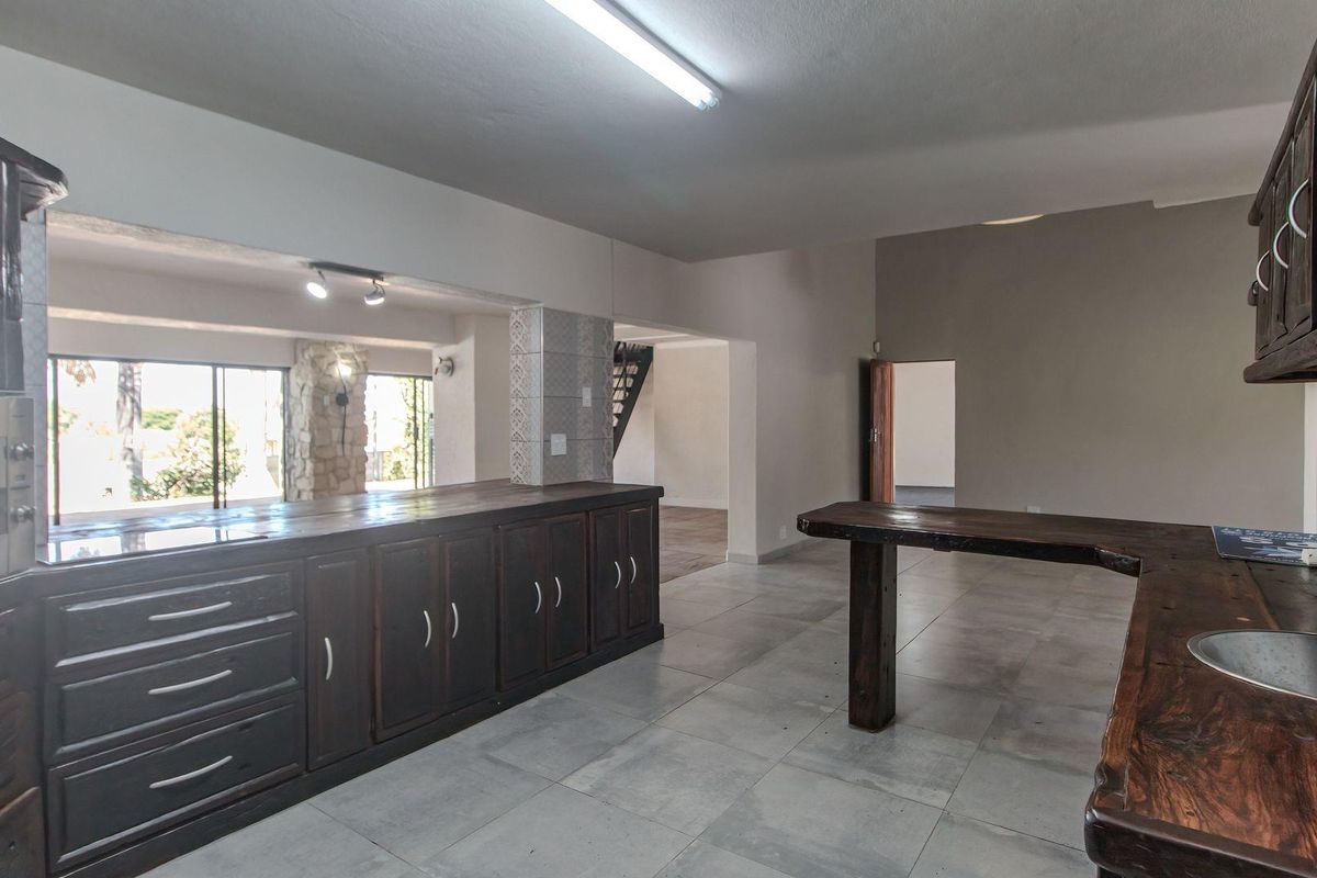 Spacious kitchen featuring dark wood cabinetry, integrated oven, and a large breakfast bar, opening into an adjacent living area with tiled flooring.