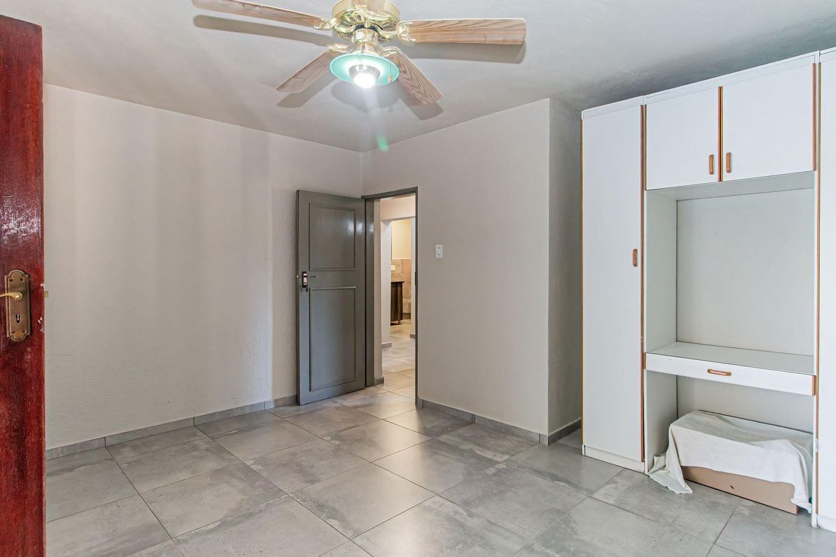 A bedroom featuring tiled flooring, a ceiling fan, and a built-in wardrobe unit with an integrated desk space.