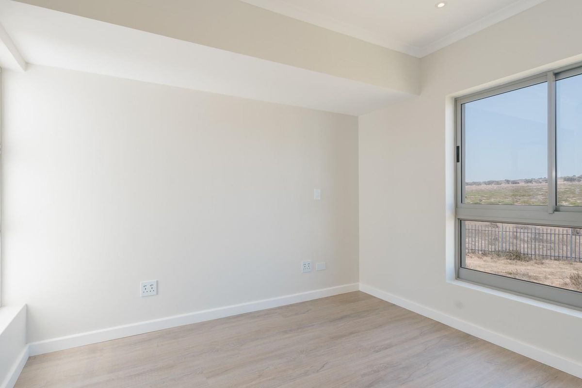 A bright, empty bedroom featuring light-toned wood-look flooring, neutral walls, and large windows offering an expansive exterior view.