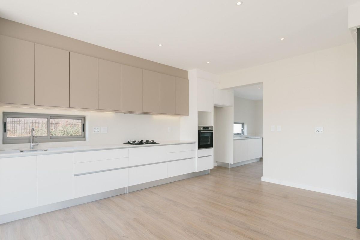 Modern kitchen featuring sleek handleless cabinetry, integrated oven, gas hob, and light wood-look flooring, with an adjacent scullery area.
