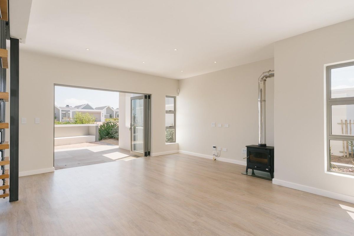 Bright and spacious living area featuring light wood-look flooring, a modern freestanding fireplace, and large stacker doors opening to an outdoor patio.