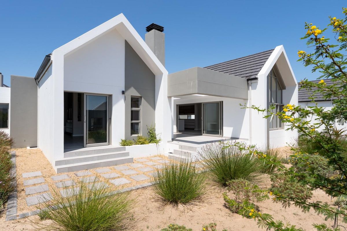 Modern architectural rear elevation featuring clean lines, a pitched roof, integrated chimney, and paved patio area leading into the home.