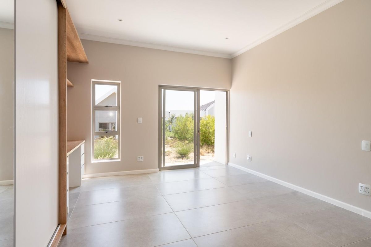 A bright, modern bedroom featuring neutral tiled flooring, built-in cabinetry, and sliding glass doors providing direct access to the garden.