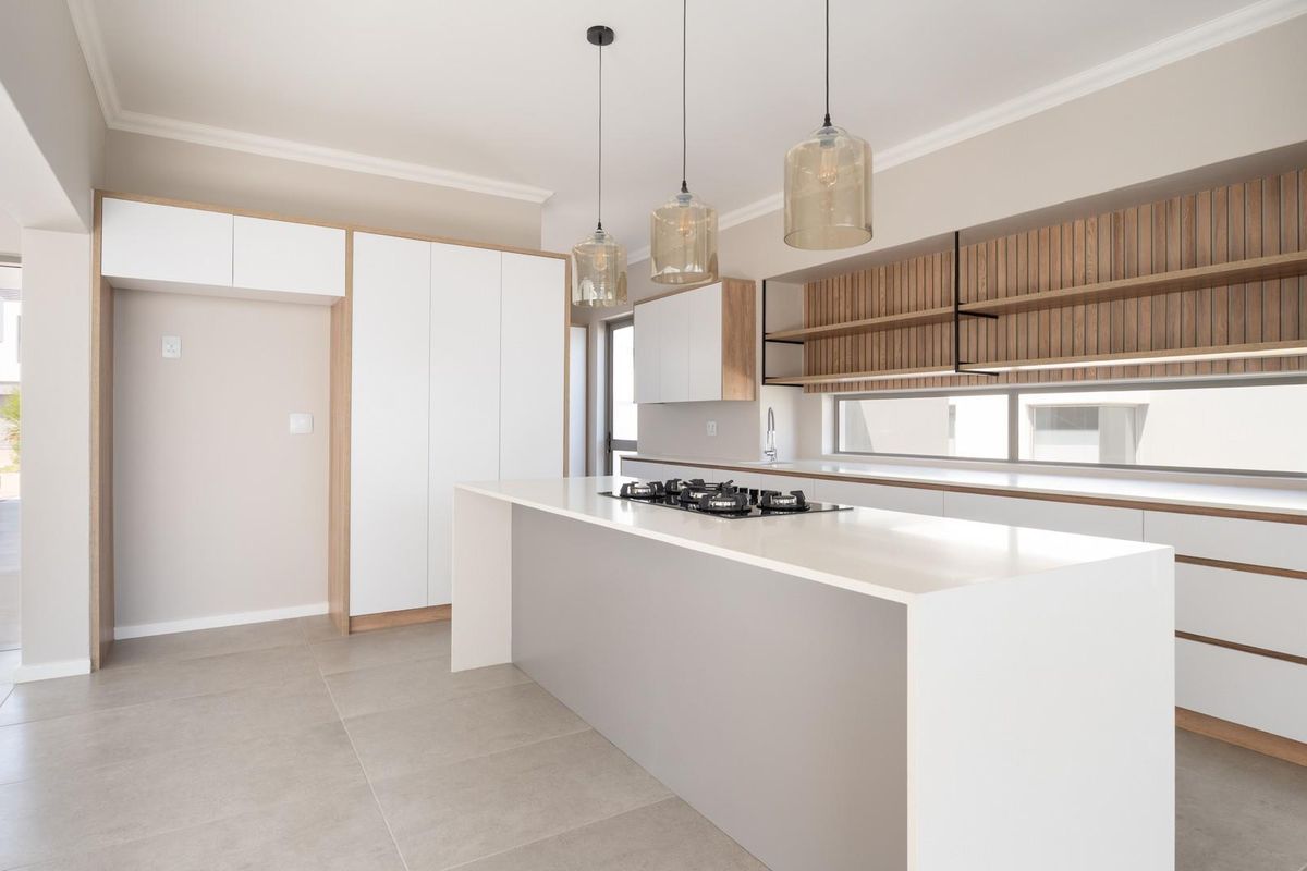 Modern kitchen featuring a central island with a built-in gas hob, sleek white cabinetry, timber-slatted wall paneling, and contemporary pendant lighting.