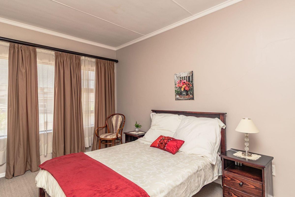 A standard bedroom featuring neutral wall tones, carpeted flooring, and large windows with curtain tracks.