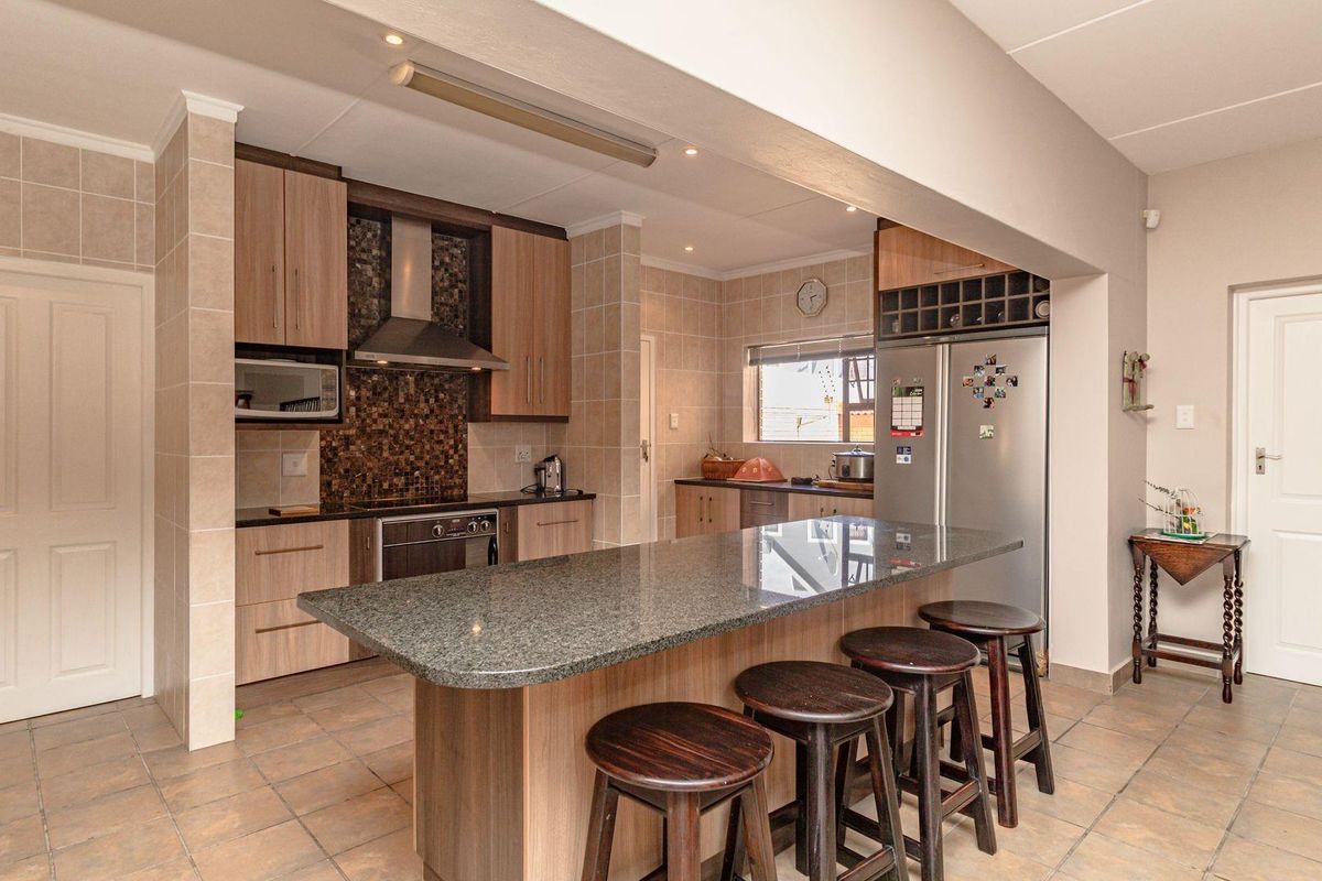 A functional kitchen featuring wood-finish cabinetry, granite countertops, a central breakfast island, and a tiled backsplash with integrated stainless steel appliances.