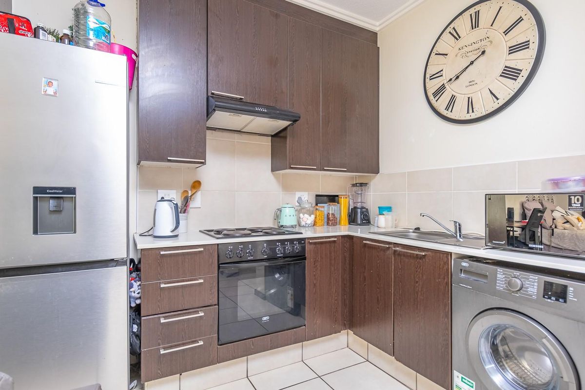 Compact kitchen featuring dark wood cabinetry, tiled backsplash, built-in oven with hob, extractor fan, and integrated space for a washing machine.