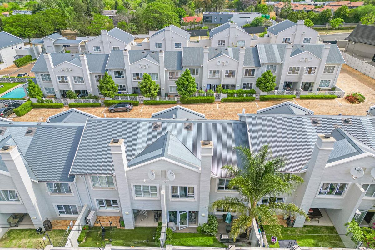 Aerial view of a townhouse complex featuring uniform architectural design, corrugated metal roofing, private rear gardens, and paved communal driveway access.