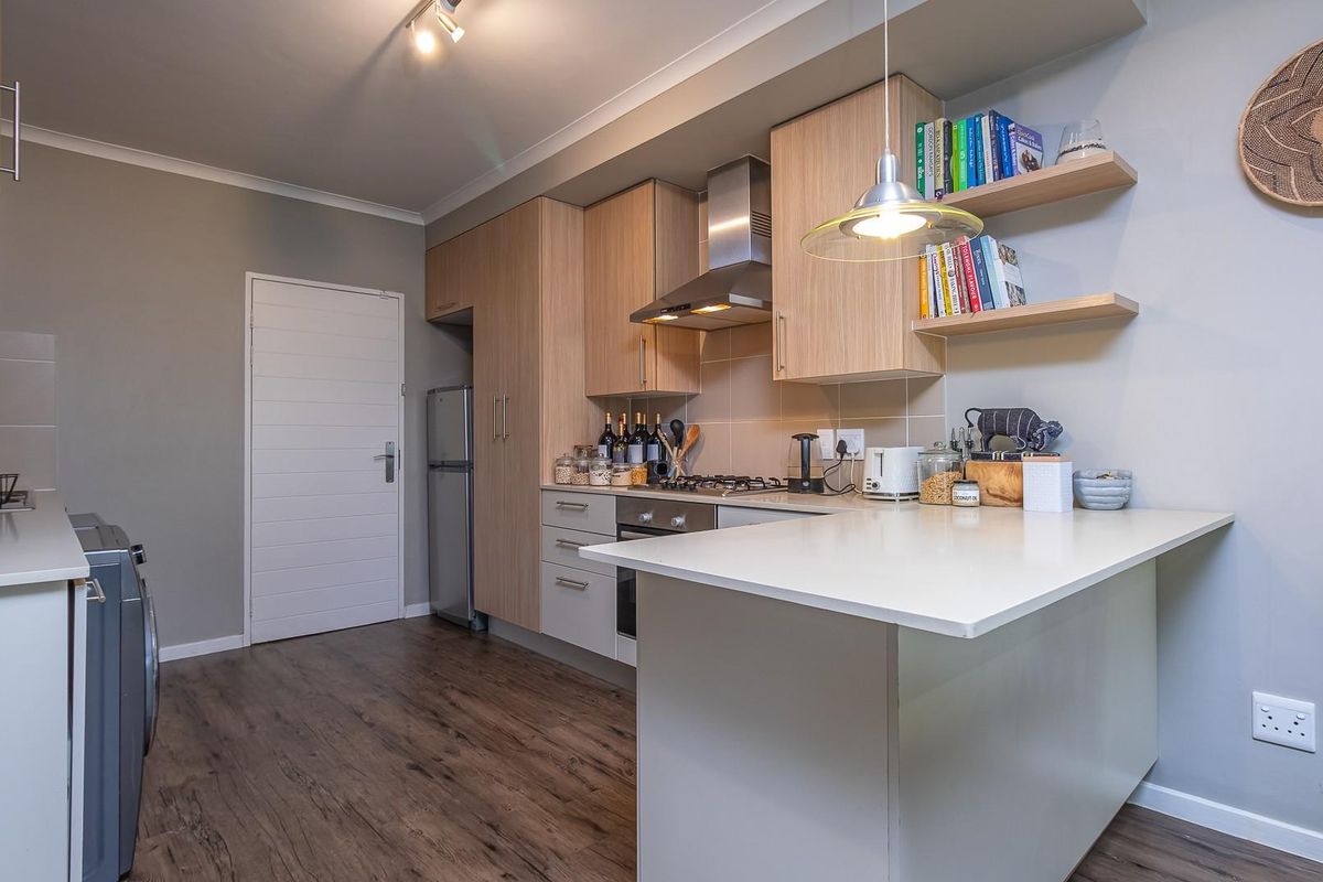 Modern kitchen featuring light wood cabinetry, stone countertops, built-in oven, gas hob, stainless steel extractor fan, and floating shelves with laminate flooring.