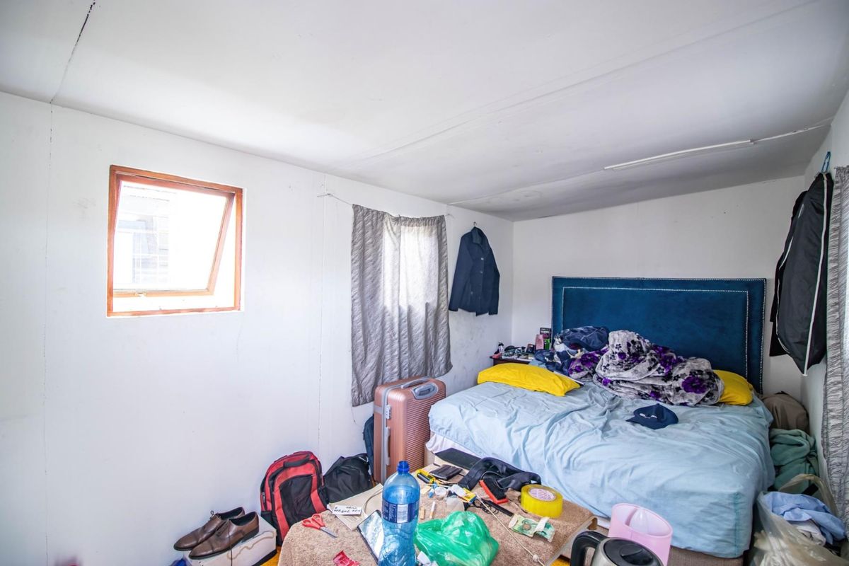 A compact bedroom featuring a blue upholstered headboard, a small top-hinged window, and basic wall finishes.