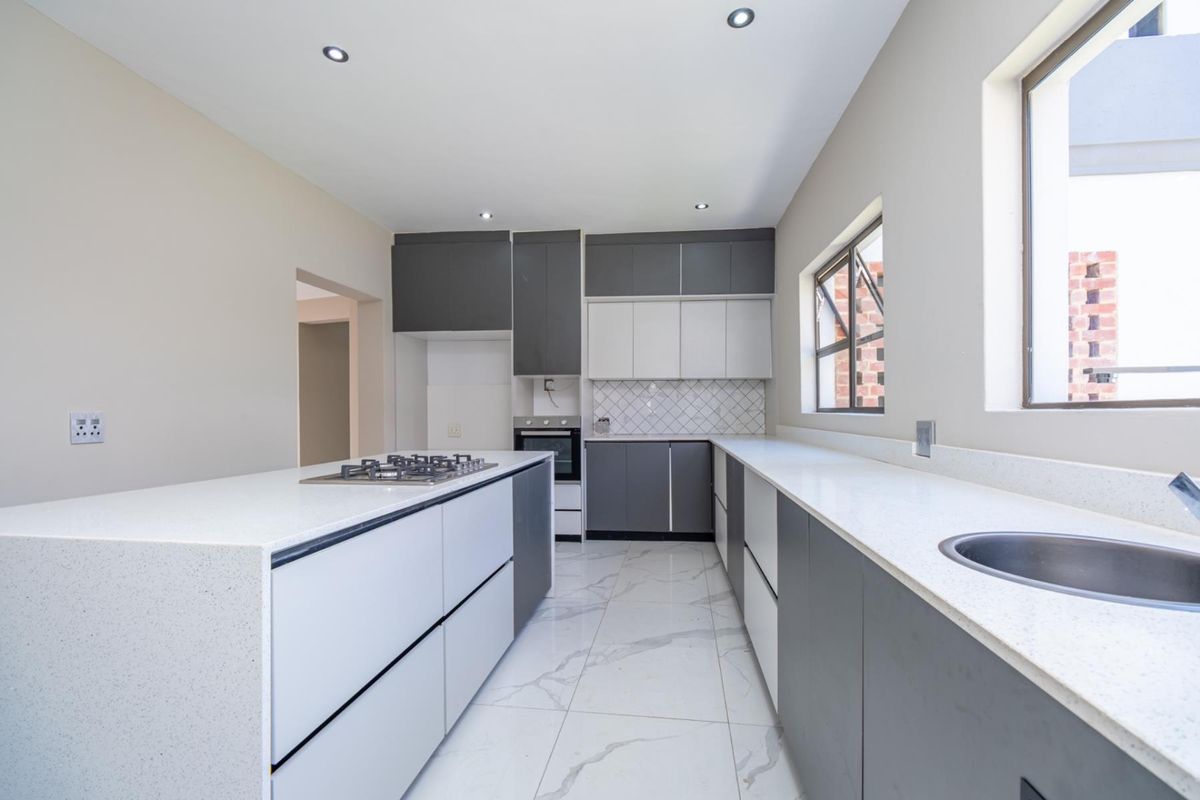 Modern kitchen featuring two-tone cabinetry, stone countertops, a central island with a built-in gas hob, and sleek tiled flooring.