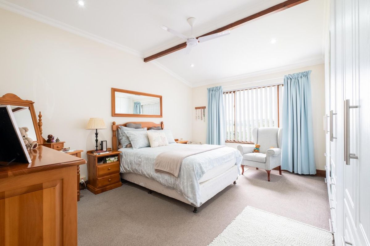 A well-maintained bedroom featuring neutral carpeting, built-in wardrobes, a ceiling fan, and large windows with vertical blinds.