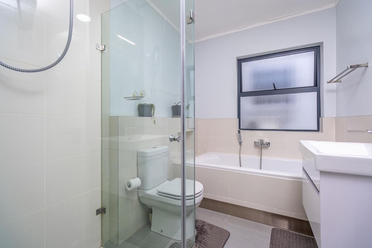 A modern, well-maintained bathroom featuring a glass-enclosed shower, a built-in bathtub, a vanity basin, and a toilet with neutral wall tiling.
