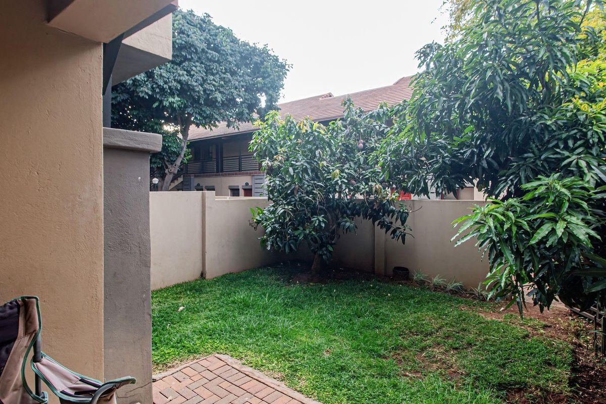 A private rear garden area featuring a paved patio section, established trees, and perimeter boundary walls, offering a secluded outdoor space.