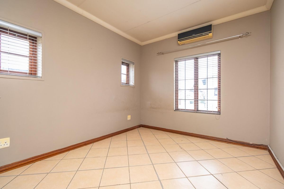 An empty bedroom featuring tiled flooring, multiple windows with fitted blinds, and a wall-mounted air conditioning unit.