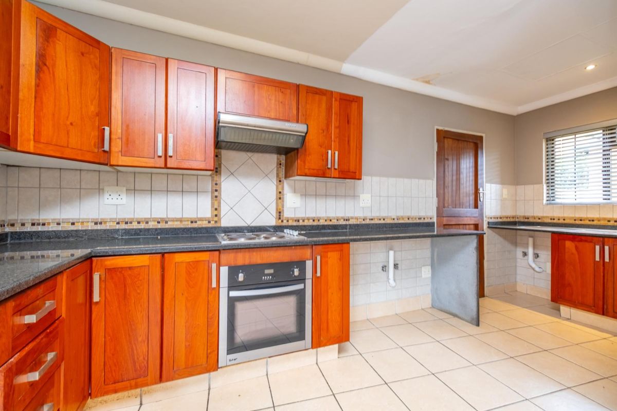 A functional kitchen featuring wooden cabinetry, granite countertops, a built-in oven, hob, and extractor fan, with tiled flooring and backsplash.