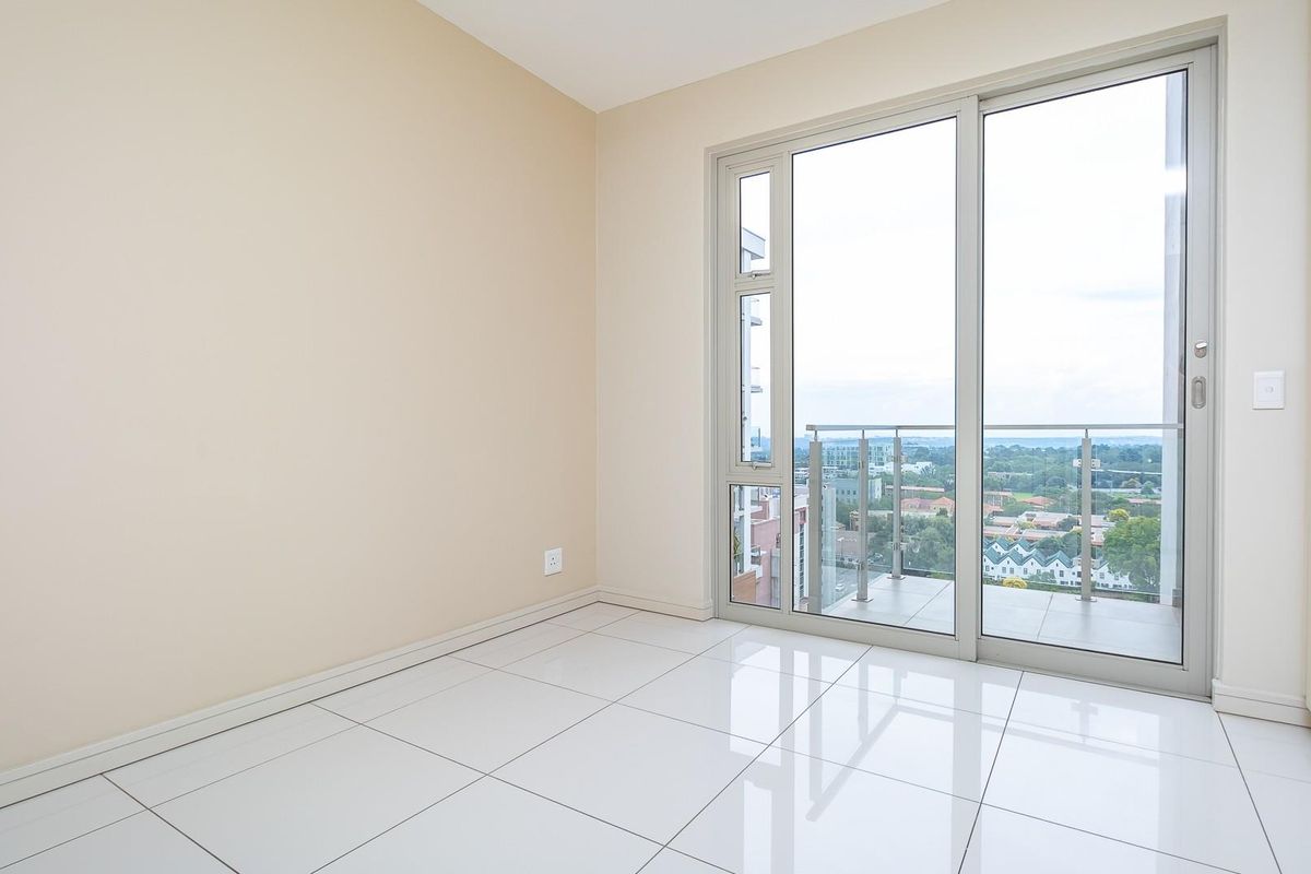 A bright, empty bedroom featuring large sliding glass doors that open onto a private balcony with expansive urban views and polished floor tiles.