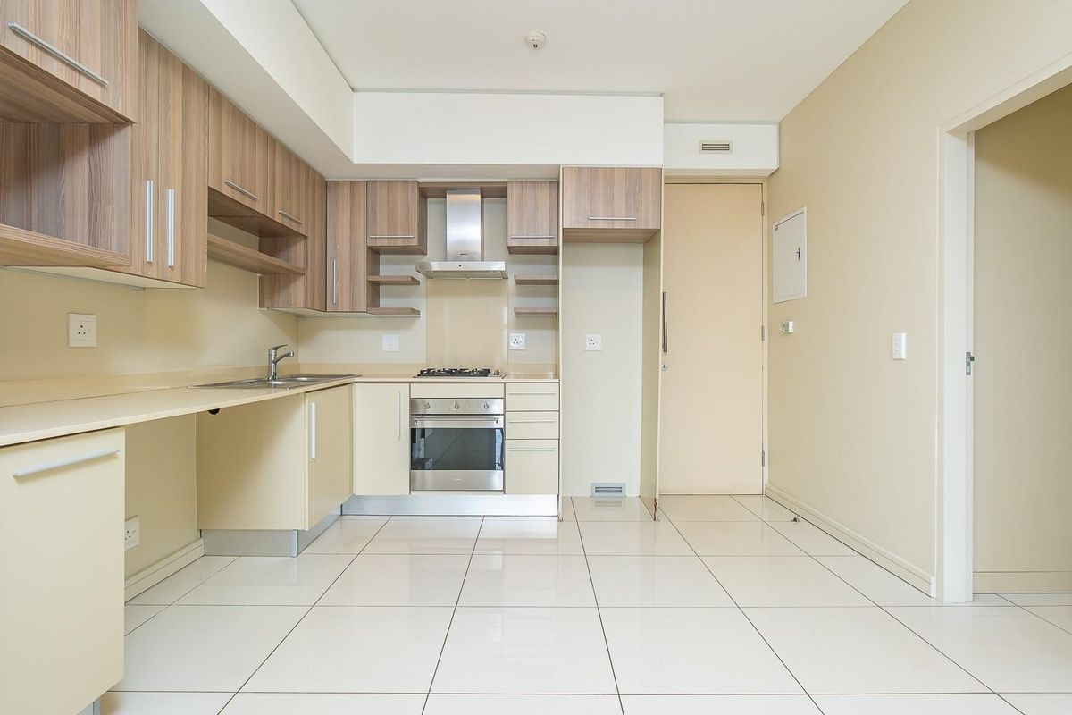 A clean, modern kitchen featuring light wood-tone cabinetry, built-in oven, gas hob, stainless steel extractor fan, and tiled flooring.