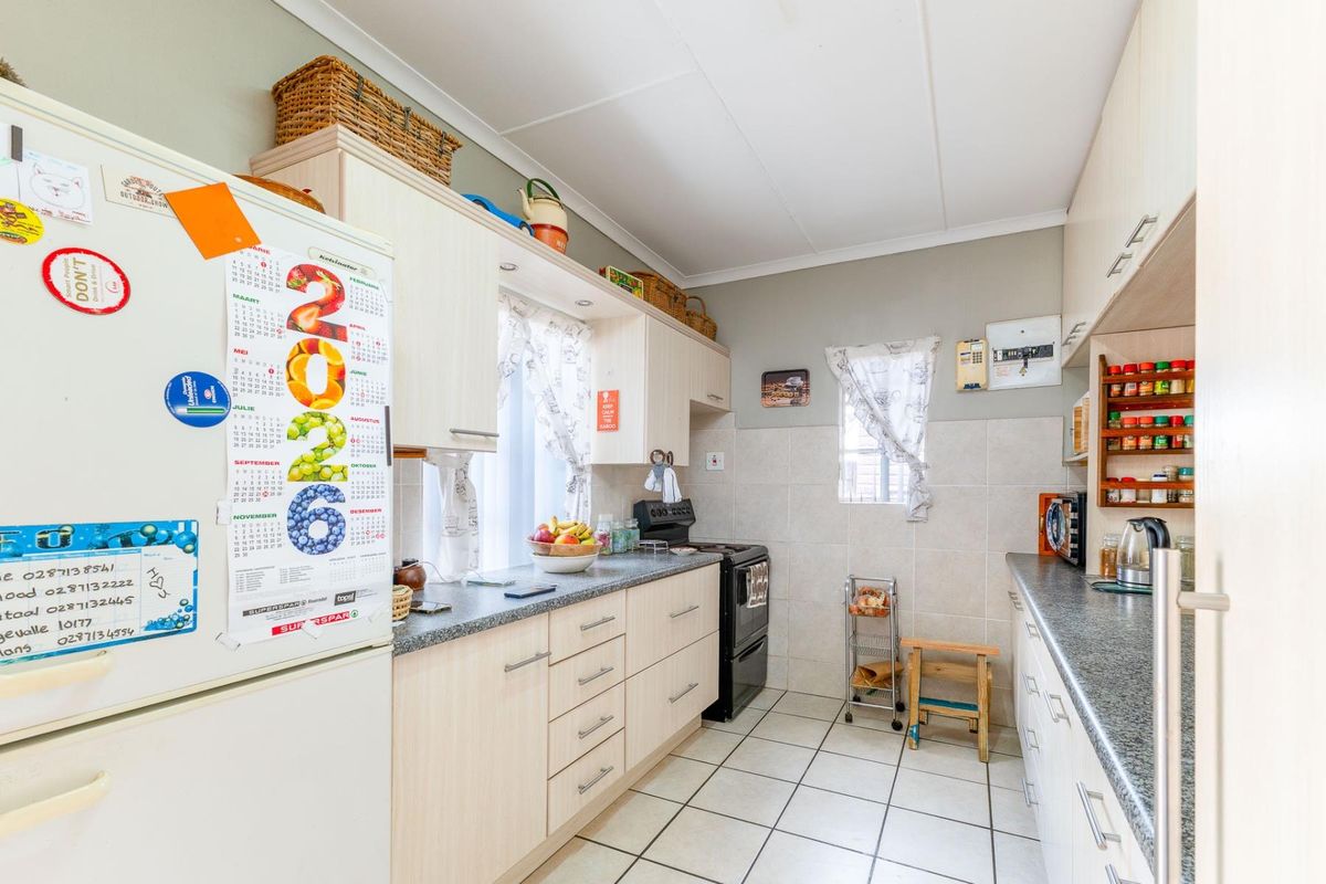 A functional galley-style kitchen featuring light-toned cabinetry, granite-look countertops, tiled splashbacks, and tiled flooring.