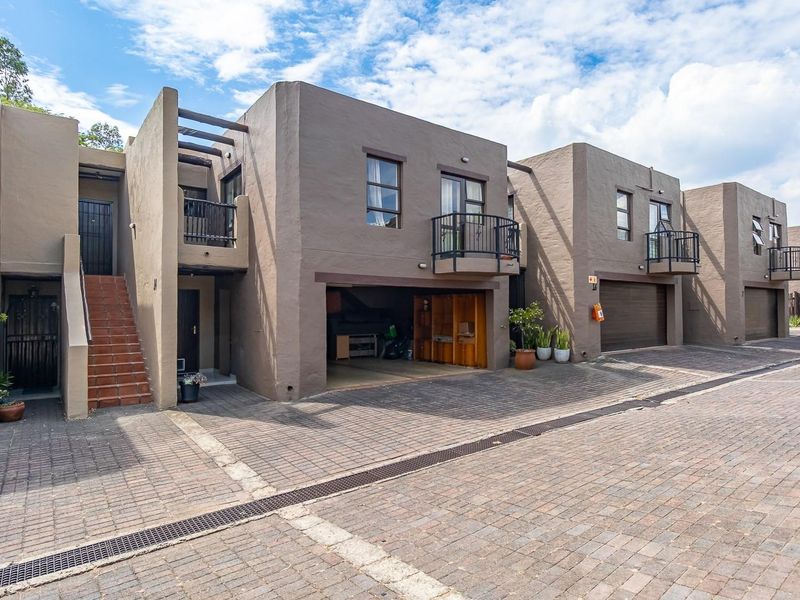 Front elevation of a townhouse complex featuring paved driveway access, integrated garages, and upper-level balconies with security features.
