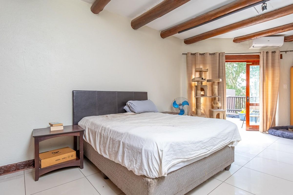 Spacious bedroom featuring exposed timber ceiling beams, tiled flooring, and direct access to a private balcony through sliding glass doors.