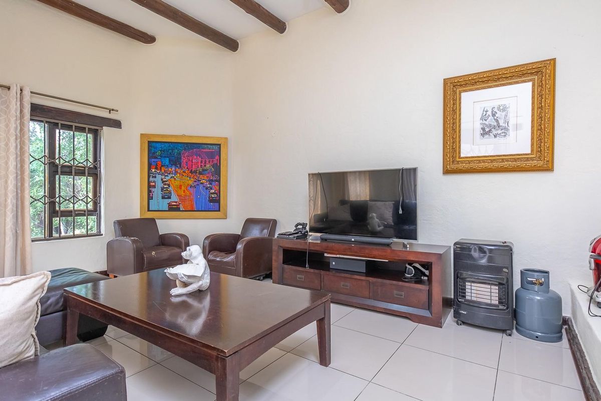 A living room featuring exposed timber ceiling beams, tiled flooring, and a window with security bars, offering a comfortable and functional living space.