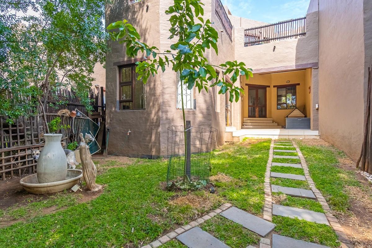 Rear view of the townhouse featuring a private garden, stone paver walkway, and an elevated balcony area with a neutral exterior finish.