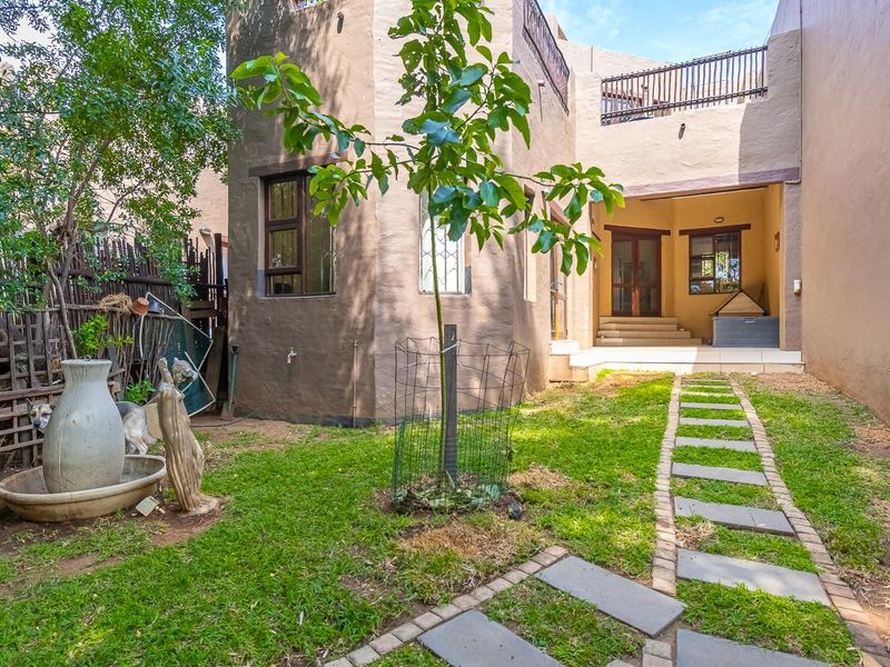 Rear view of the townhouse featuring a private garden, stone paver walkway, and an elevated balcony area with a neutral exterior finish.