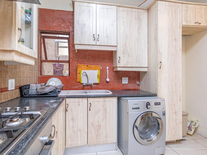 Functional kitchen featuring light wood-finish cabinetry, granite countertops, a gas hob, and a vibrant red mosaic tile backsplash.